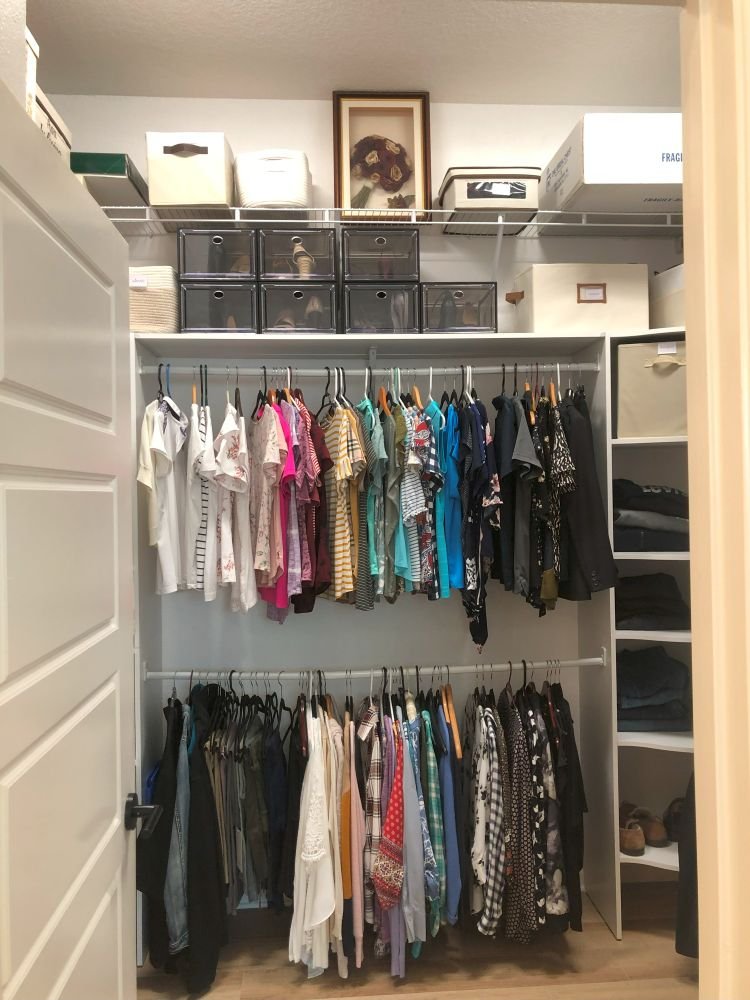 Center view of a neatly organized closet with color-coded clothing, labeled storage bins, and folded jeans—showing how to declutter effectively.