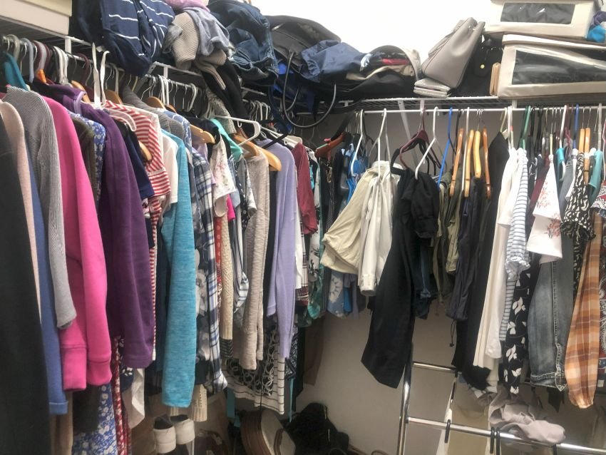 Overfilled closet with clothes tightly packed on mismatched hangers, laundry bags below, and miscellaneous items stored overhead. It's a classic example of a space in need of decluttering—hard to navigate, visually chaotic, and inefficiently organized.