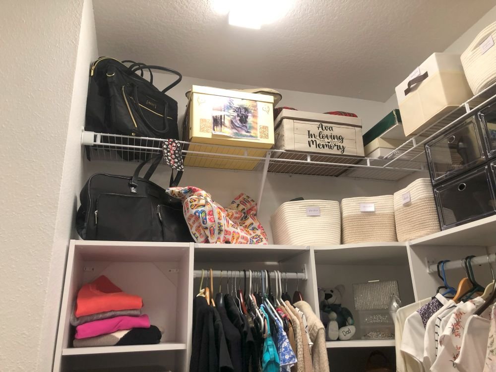 A well-organized closet with labeled bins, handbags, and a memory box stored neatly on top shelves—maximizing space while preserving personal items.