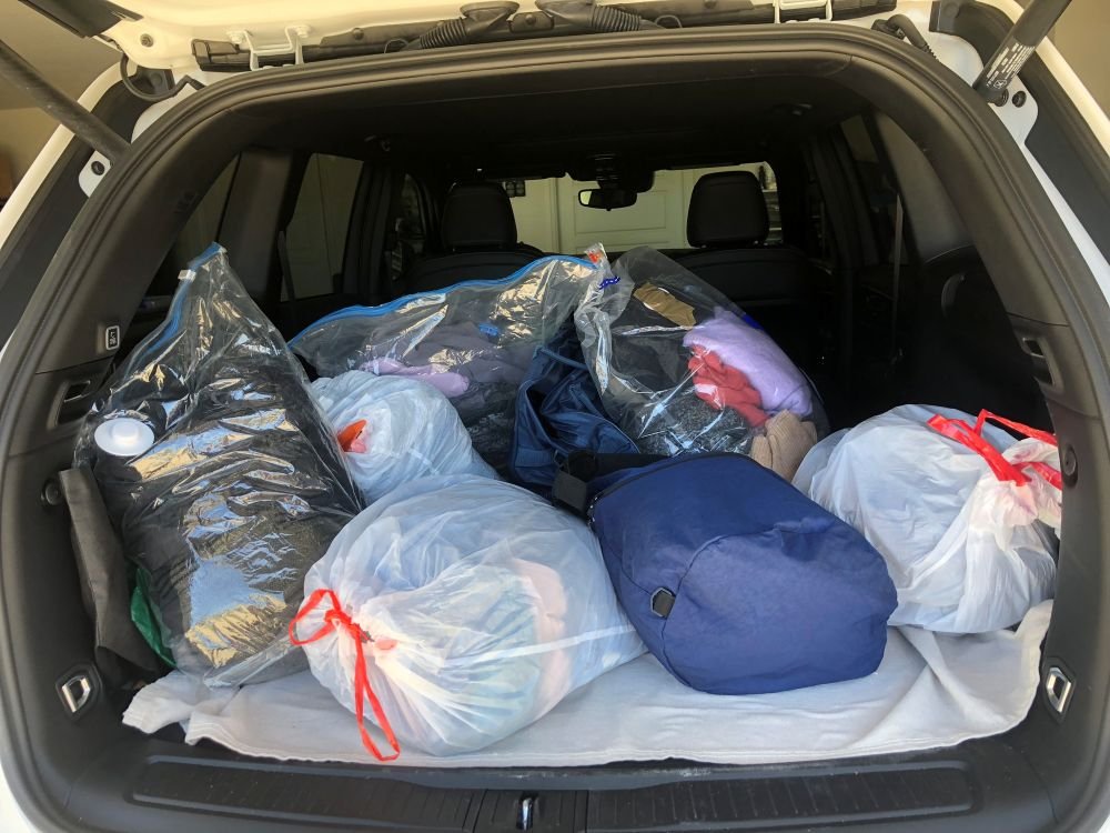 Trunk filled with bags of donated clothes packed and ready for delivery to a donation center.